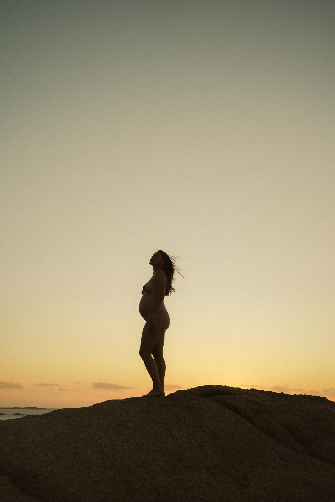 Silhouette of a pregnant woman standing on rocks at sunset