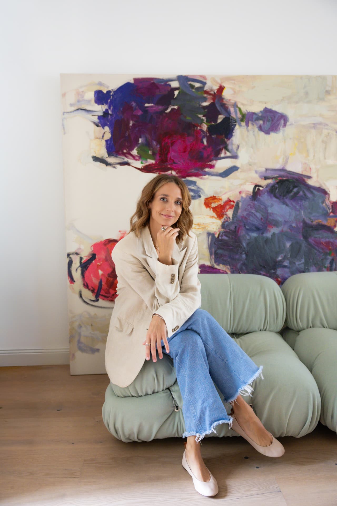Woman in a beige blazer sitting on a green sofa in front of a colorful painting