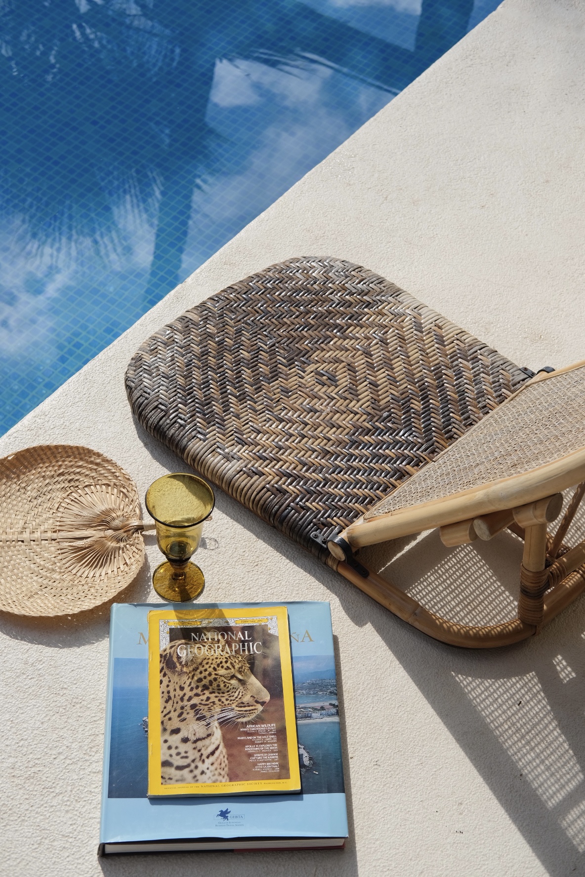 Rattan lounger, straw fan and travel books at the edge of a pool
