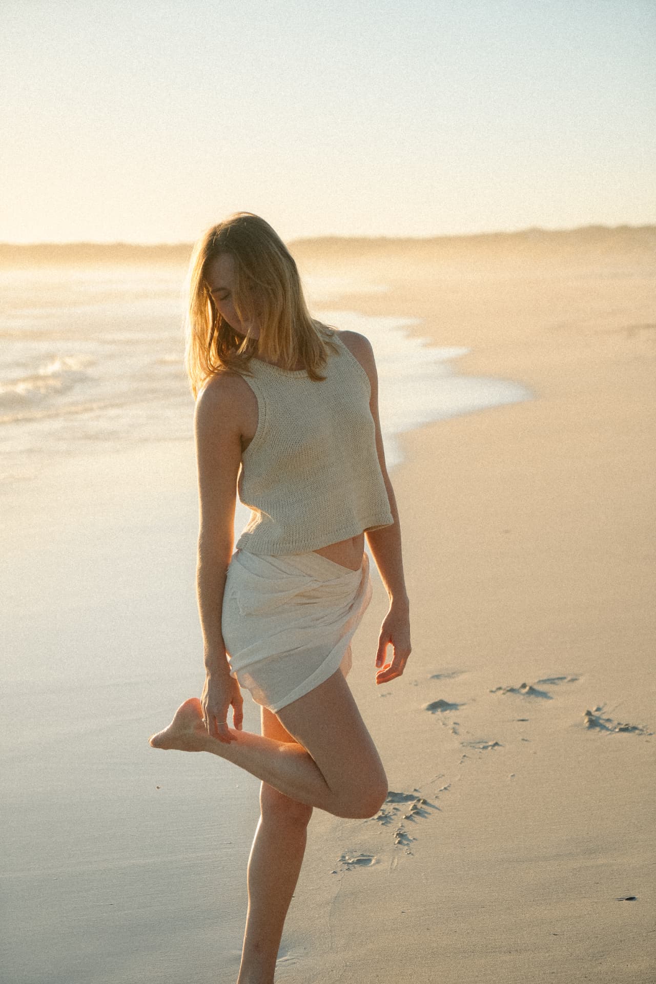 Model in a natural knit outfit posed on a sandy beach at golden hour