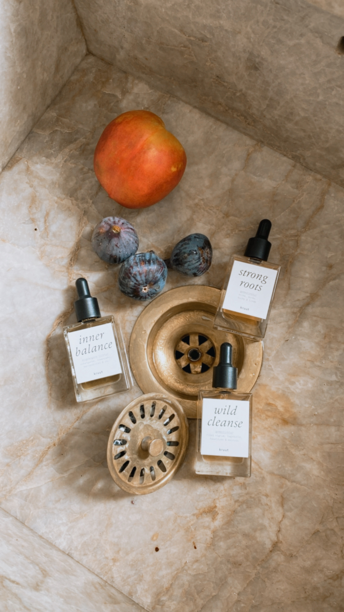 Natural skincare bottles in a stone sink styled with peach and figs