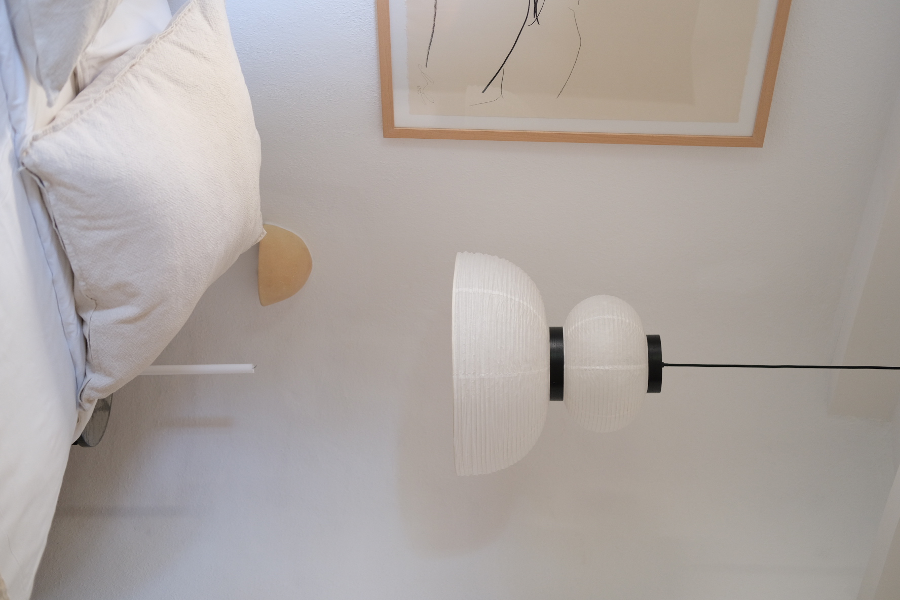 Paper pendant lamp above a bed with linen pillows and framed line drawing
