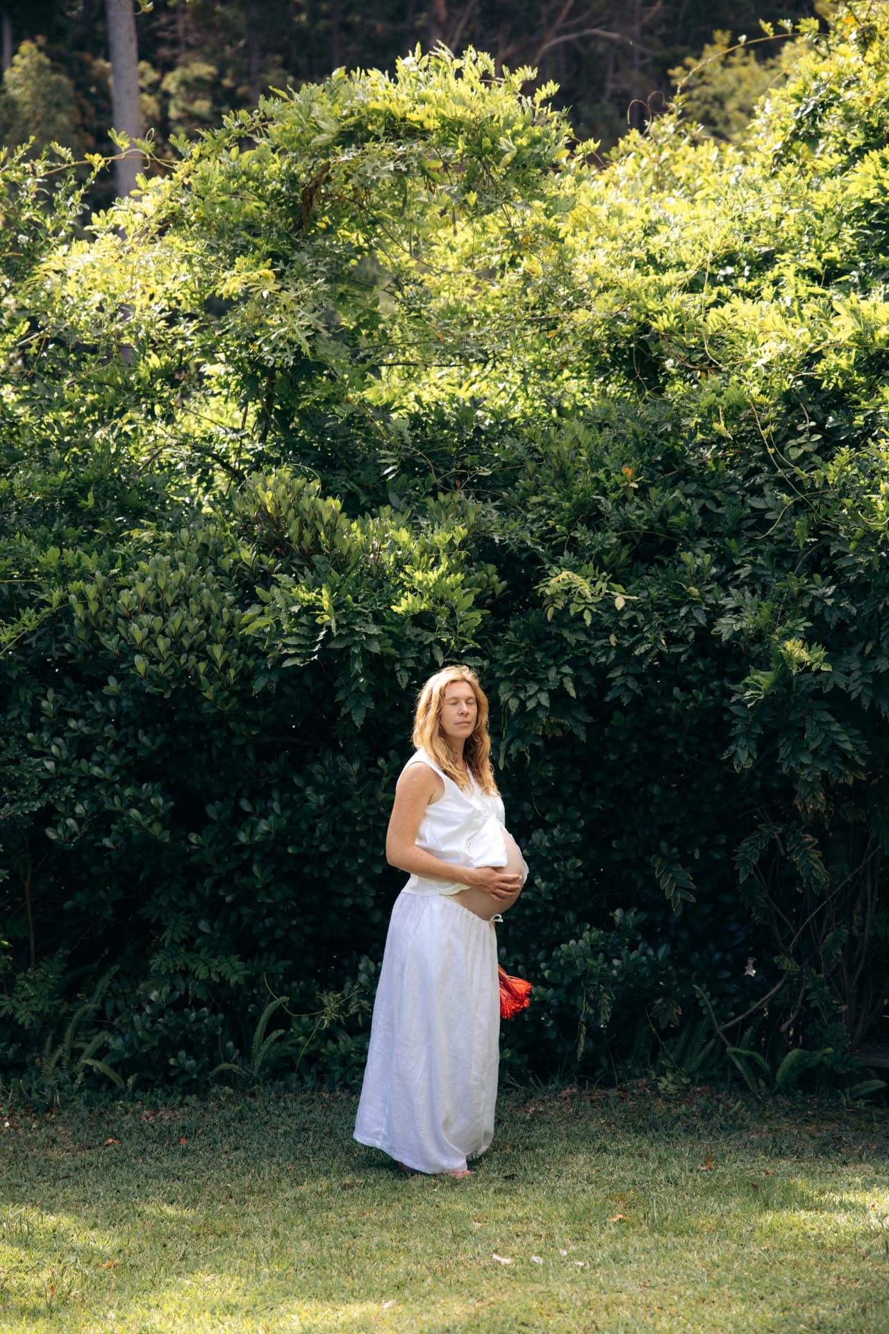Pregnant woman in a white dress standing in a green garden