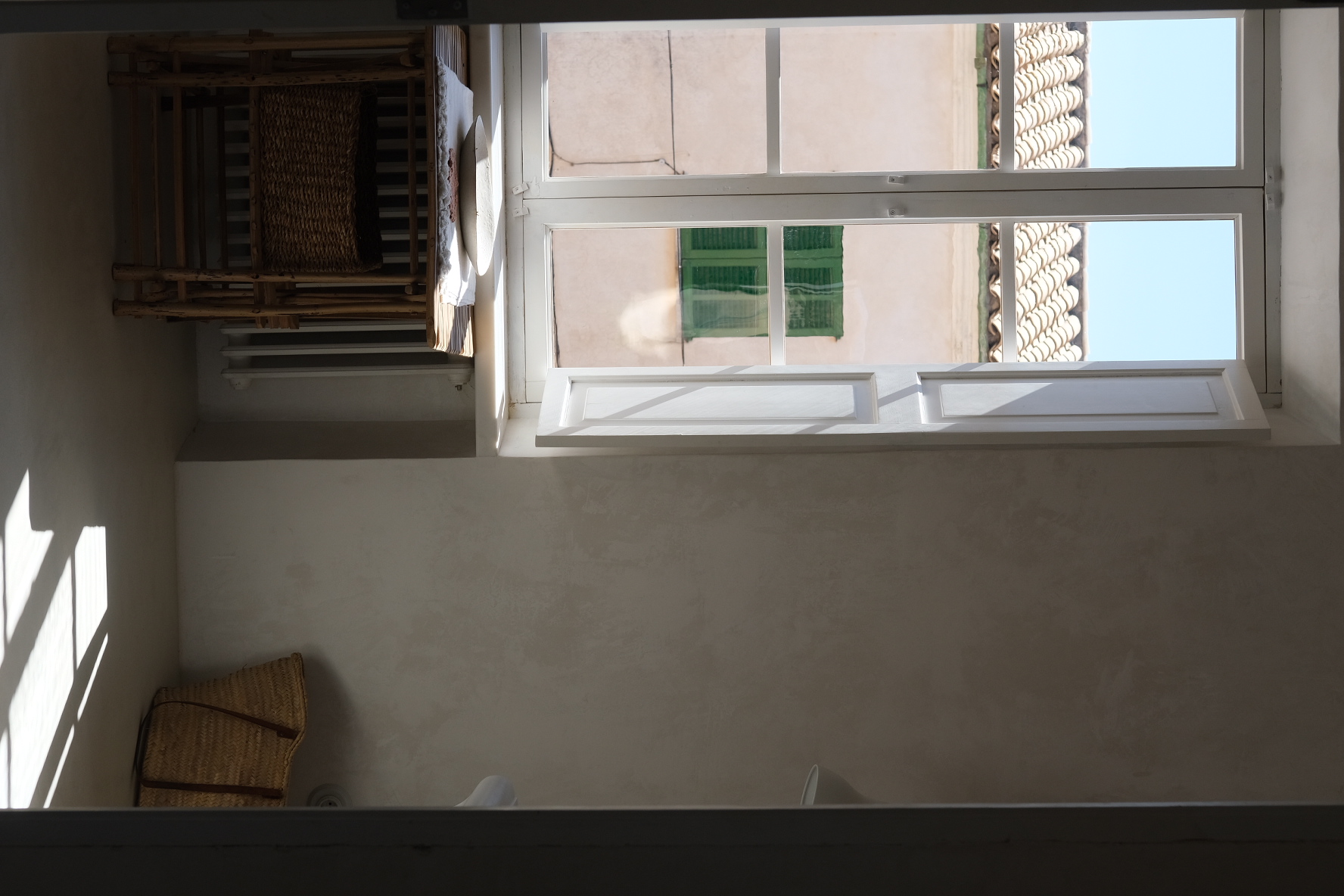Sunlit room with a white multi-pane window casting sharp shadows beside a cane shelving unit
