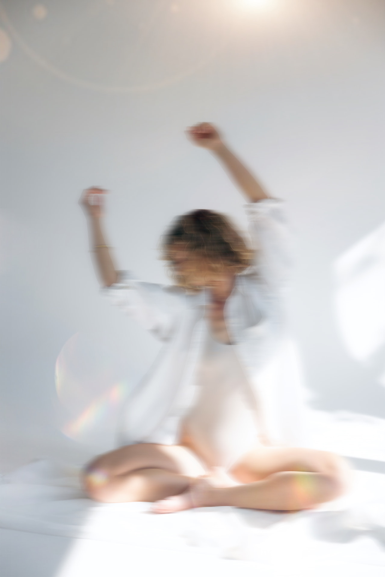 Woman lying on the floor in brown linen, arms stretched above her head in sunlight