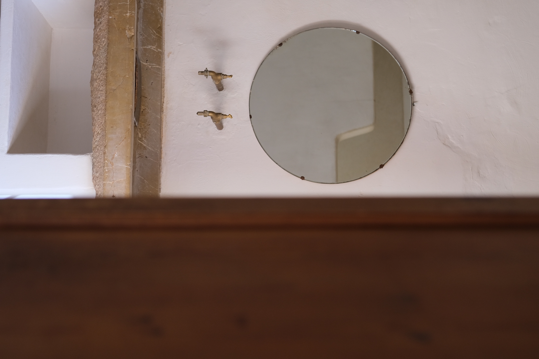 Round mirror above a stone basin with brass taps, seen through a doorway