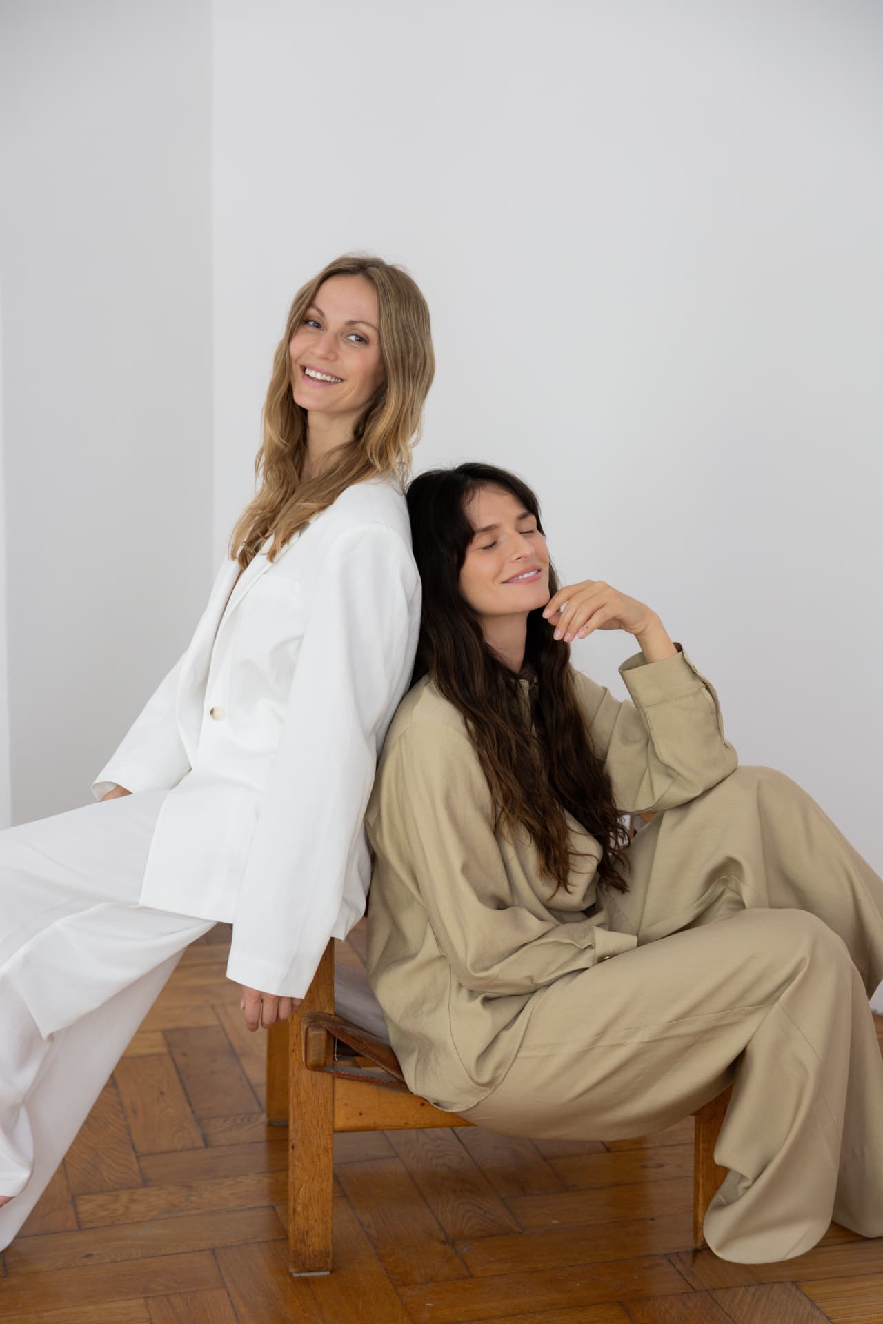 Two women sitting back to back, laughing, in white and beige