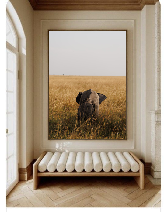 Golden Grass elephant print in a large frame above a white bench in a bright hallway