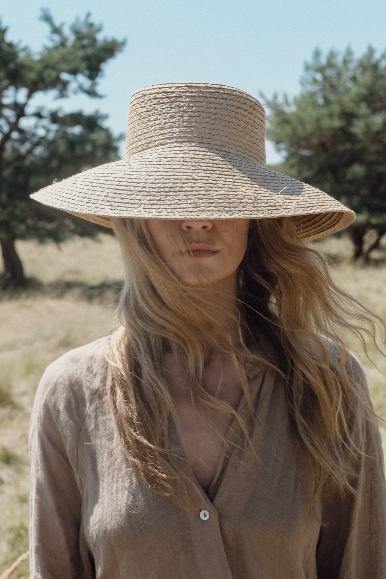 Woman in a wide-brimmed straw hat and linen blouse in dry summer grassland