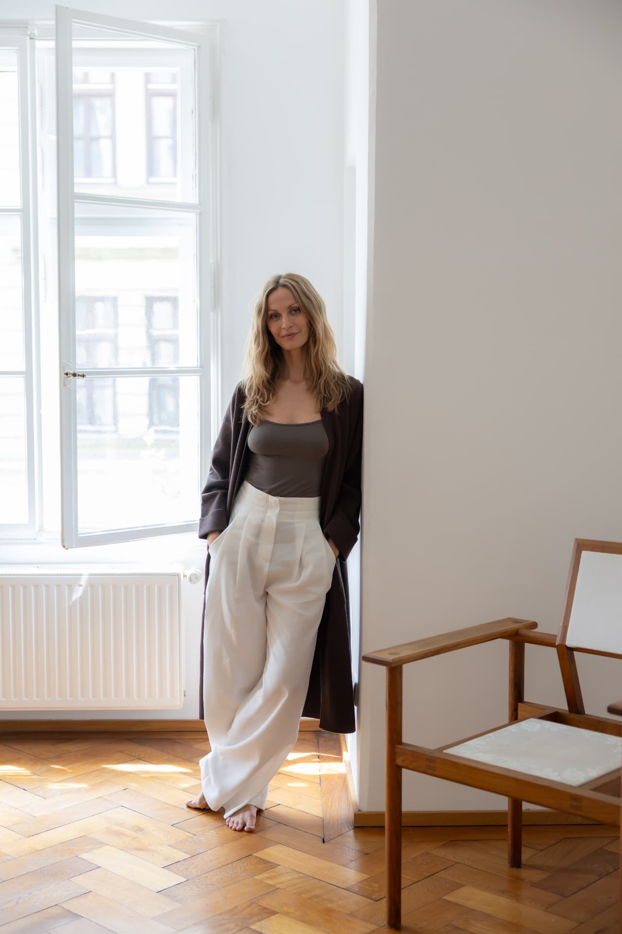 Woman leaning against a bright window wall in wide white trousers