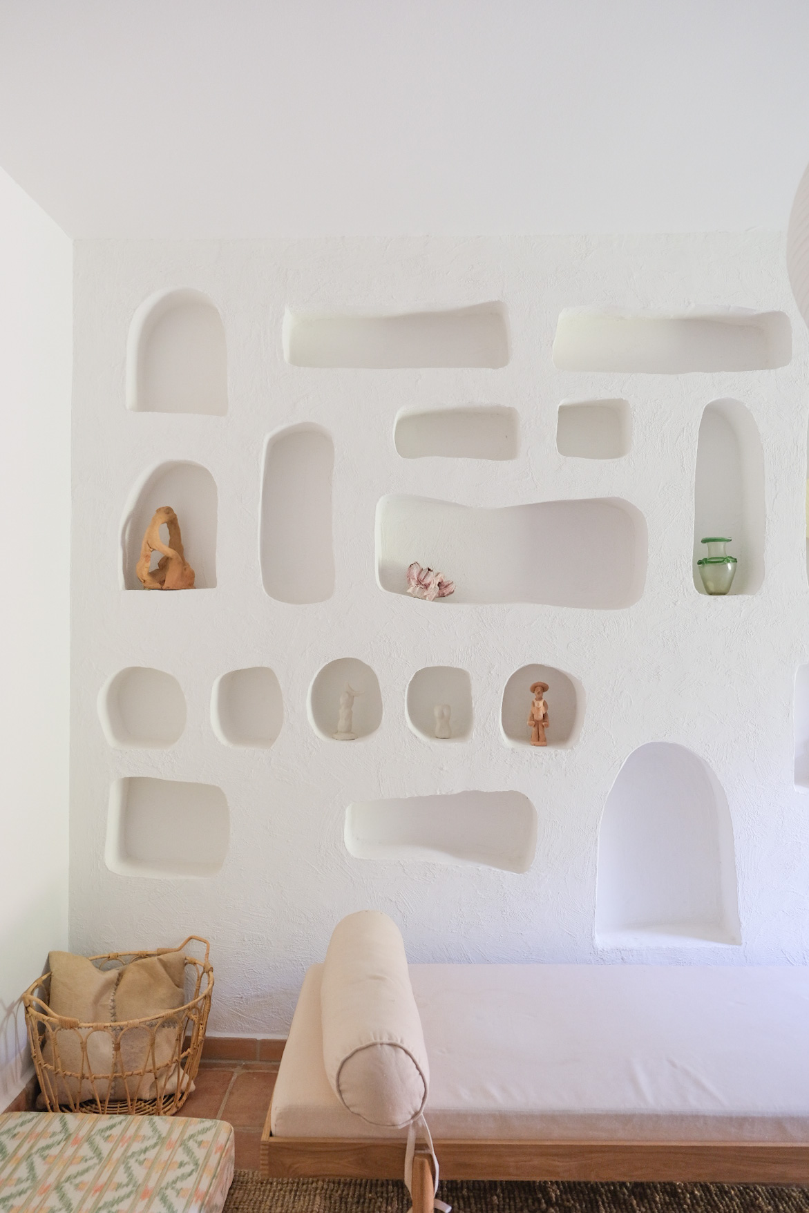 Whitewashed wall of plastered niches with clay figures and a daybed