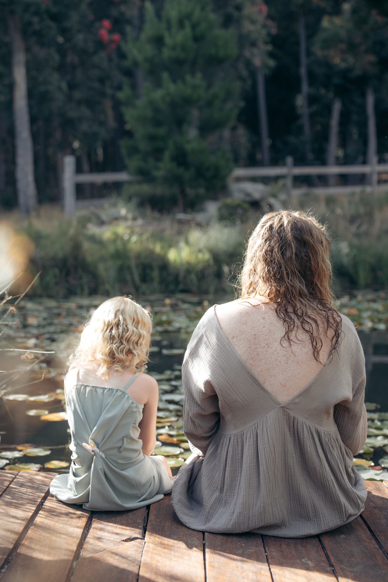 Woman and girl sitting on a wooden dock overlooking a pond
